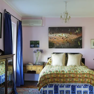 Quaint bedroom with baby pink walls, a double bed with woven quilt, and antique mahogany cabinets.