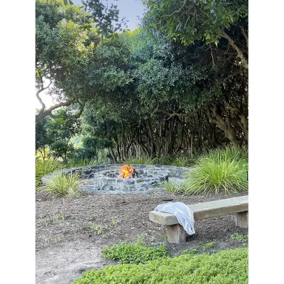 Outdoor fire pit with cement bench and surrounded by luscious green garden.