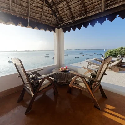 Outdoor patio with wicker chairs facing the expansive Indian Ocean scattered with traditional wooden dhows.