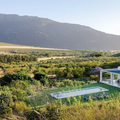 Buchubos Villa perched on a hill with a green rolling lawn and large swimming pool, and surrounded by Banghoek nature reserve and distant mountain ranges.