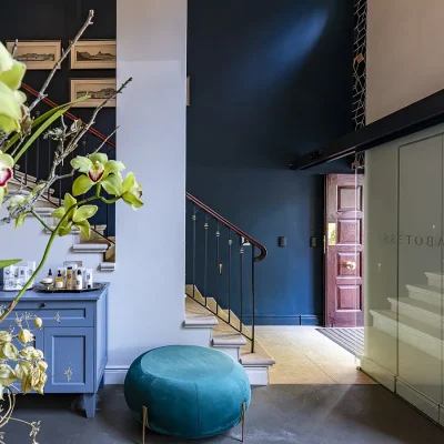 Labotessa Hotel entrance lobby with azure wooden cabinets and a matching azure ottoman, and a white stair case with navy blue walls.