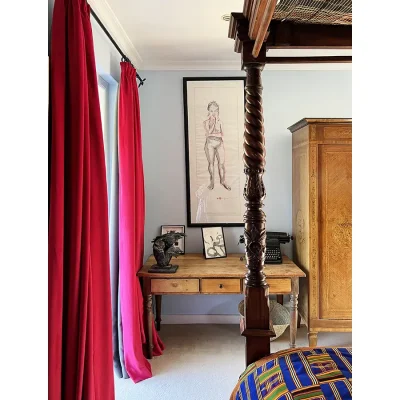 Bedroom in Villa Toscana with baby blue walls and a painting with a sketch of a lady above a wooden desk, and an antique wooden cabinet.