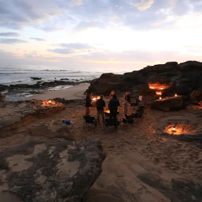 Large fire fit on the beach protected by large rock formations and overlooking the evening sky reflecting on the ocean. De Hoop Nature reserve.