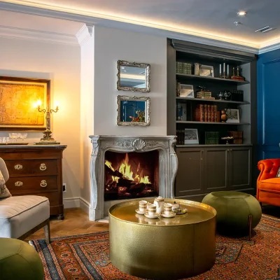 Relaxed mezzanine, with a roaring fire and muted coral velvet sofa and a wooden book case welcomes guests in an intimate low-ceilinged space in Labotessa Hotel.