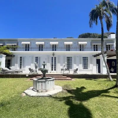 Back garden of Villa Toscana with a large water fountain in the middle of the garden complimenting the impressive whitewashed home with long windows with white awning and white wooden shutters.